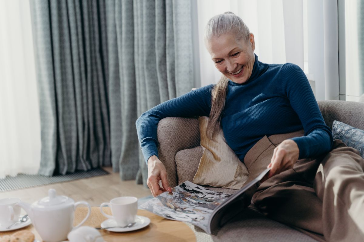 An older woman relaxing at home with a magazine and a cup of tea