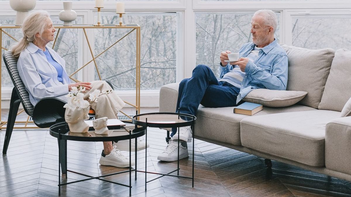 An older couple relaxing together at home in a bright, light-filled living room