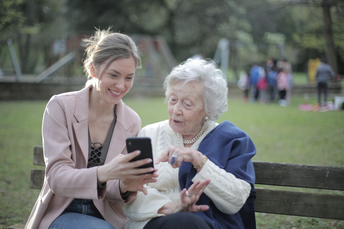 A senior mother and her adult daughter looking at a smartphone together outdoors