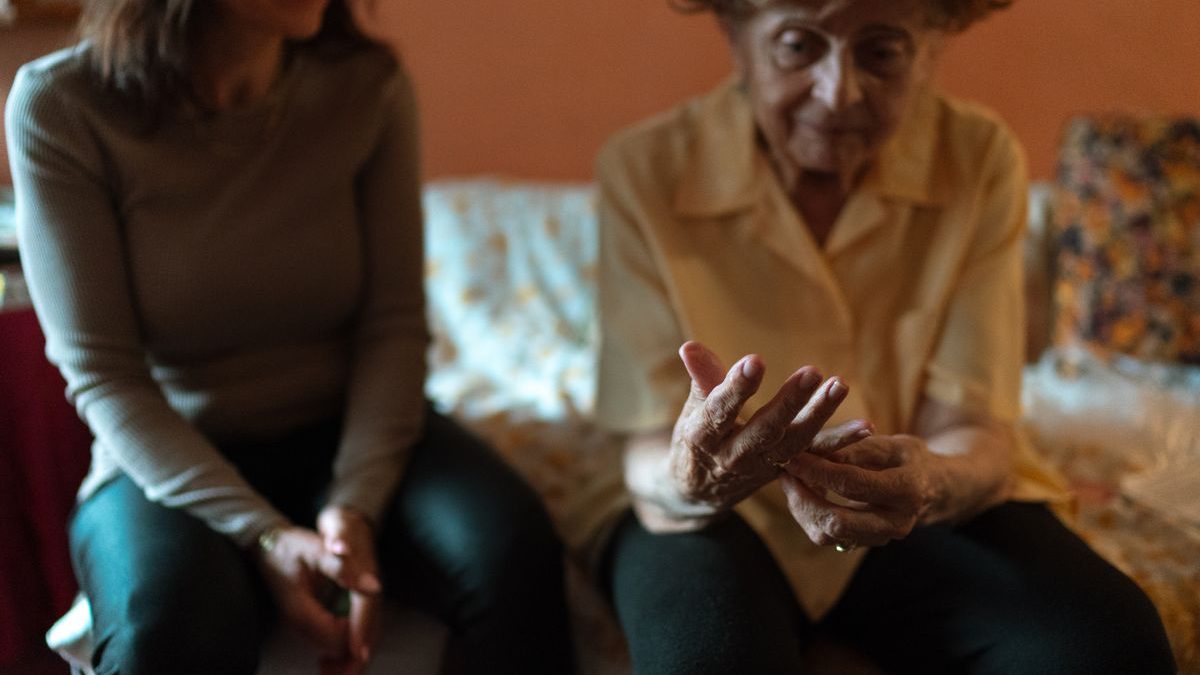 An older woman easing her hands as a family member sits with her at home