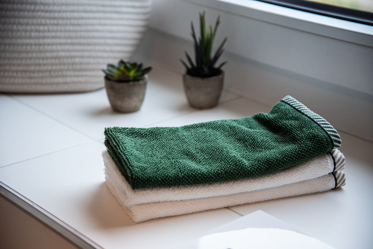 Folded towels on a bathroom counter beside two small potted plants