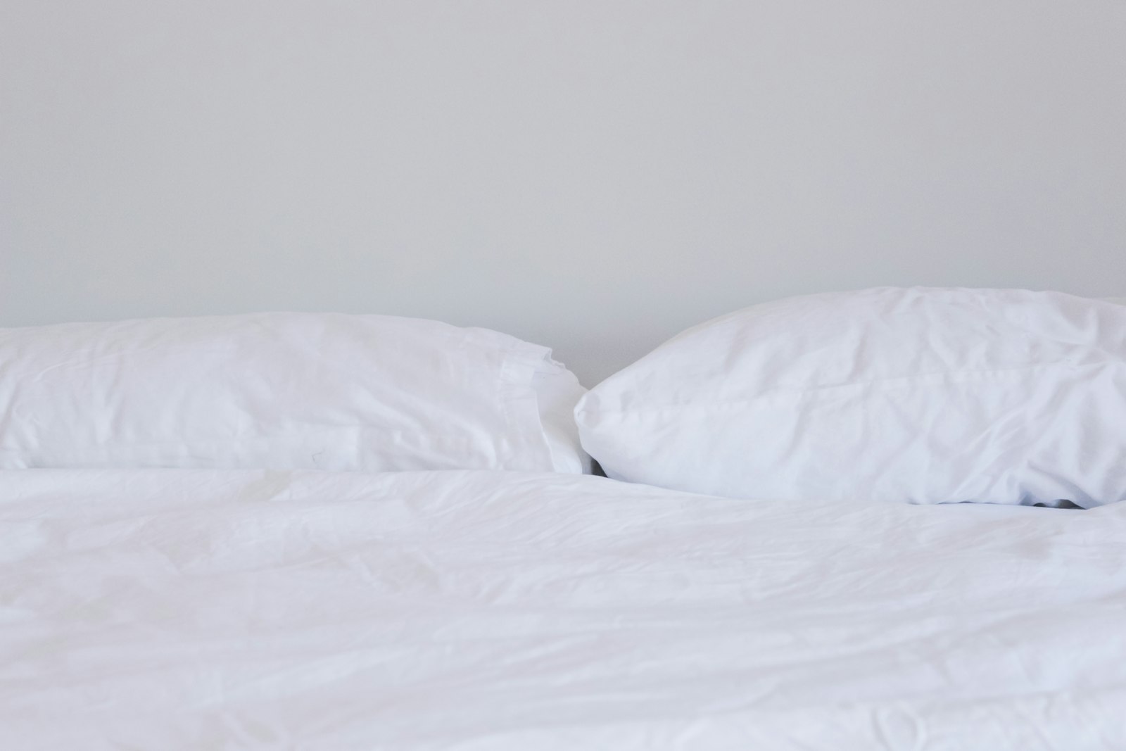 Two white pillows and a white duvet against a pale wall