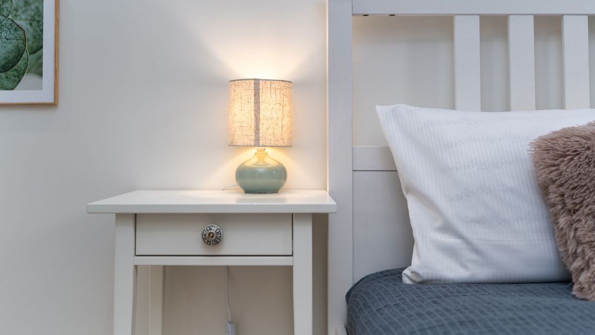 A cozy bedroom with a made bed and a warm bedside lamp