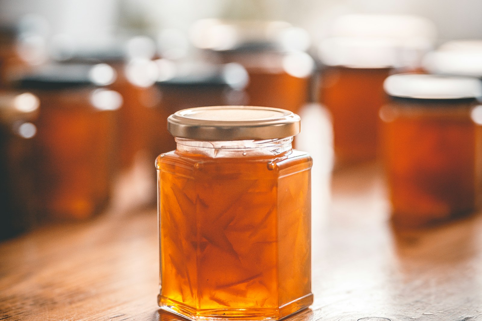 Jar of marmalade with a gold screw lid on a wooden table, more jars blurred behind