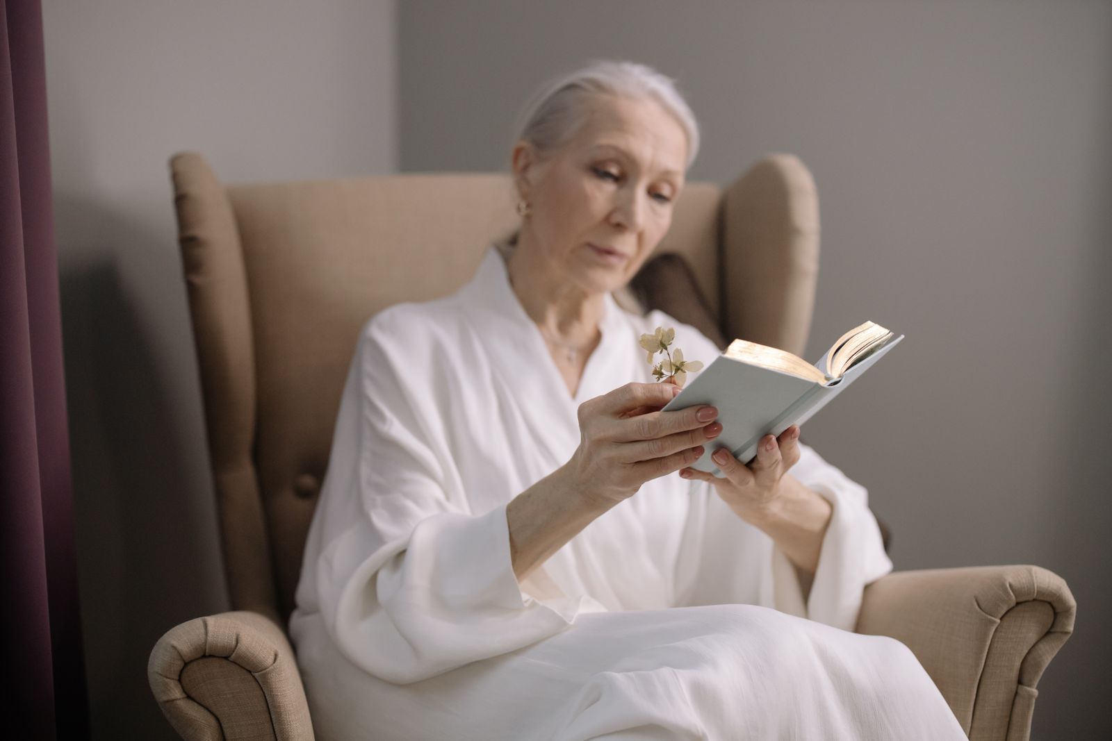 An older woman reading calmly in a comfortable upholstered armchair in a bright room, the kind of independence a good lift chair helps protect