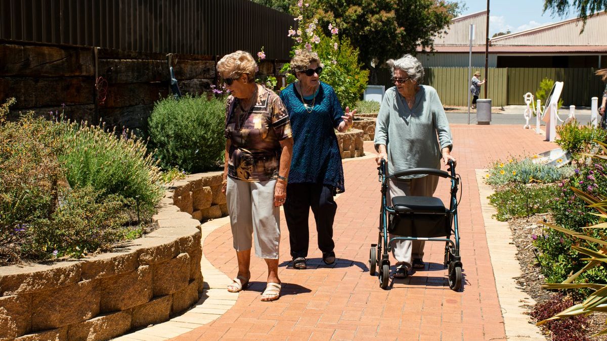 Older adults walking outdoors together, one of them using a rollator