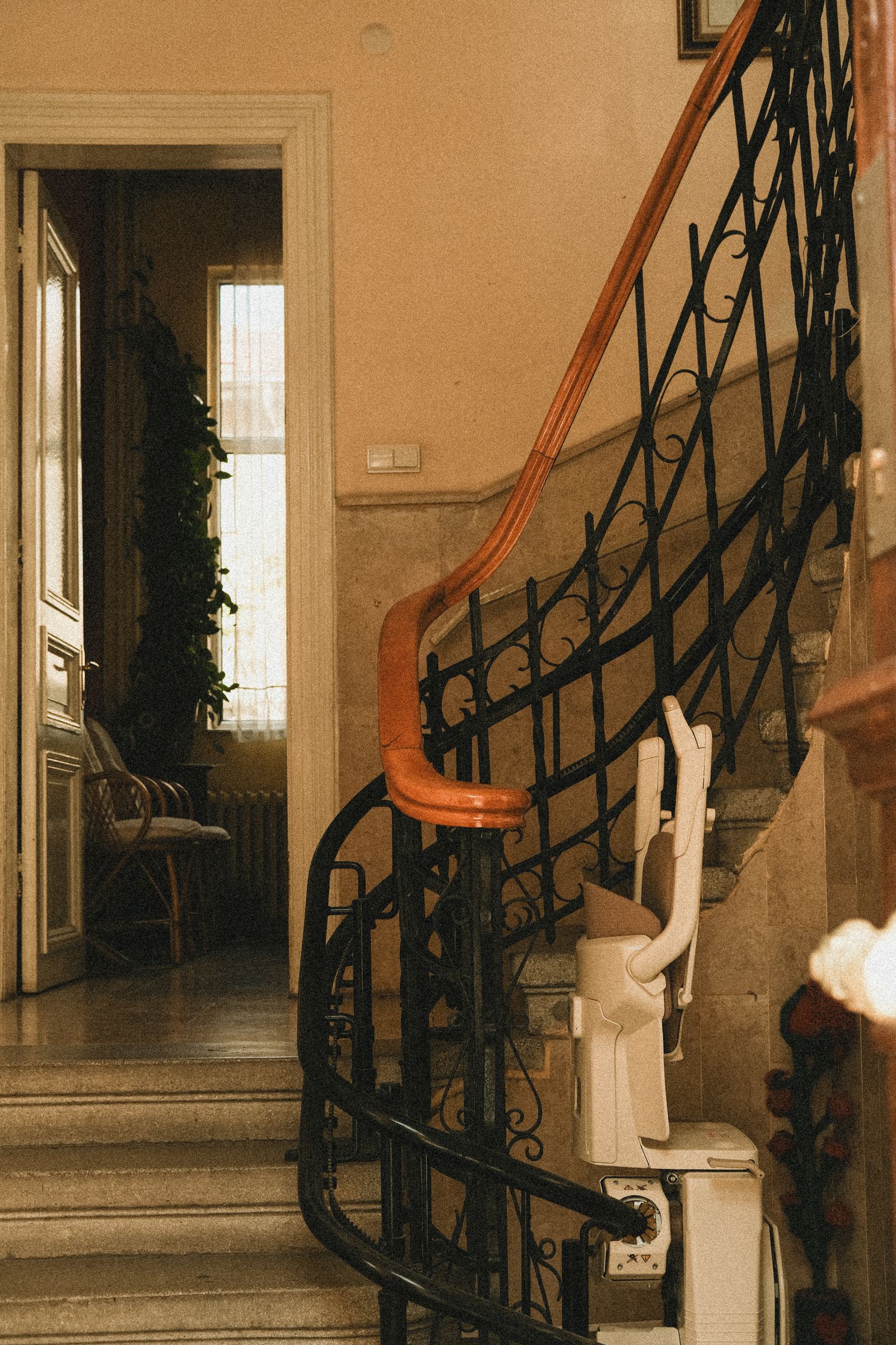 A stair lift parked at the foot of a curved staircase in a warm older home