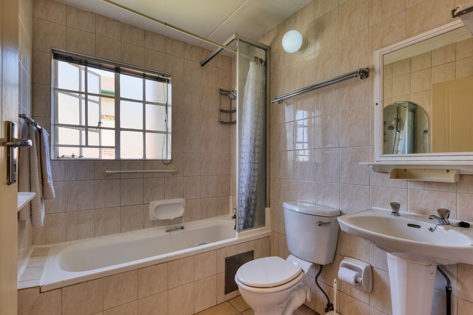 A bright home bathroom with a built-in tub and a grab bar by the window, the kind of safer bathing setup aging in place protects