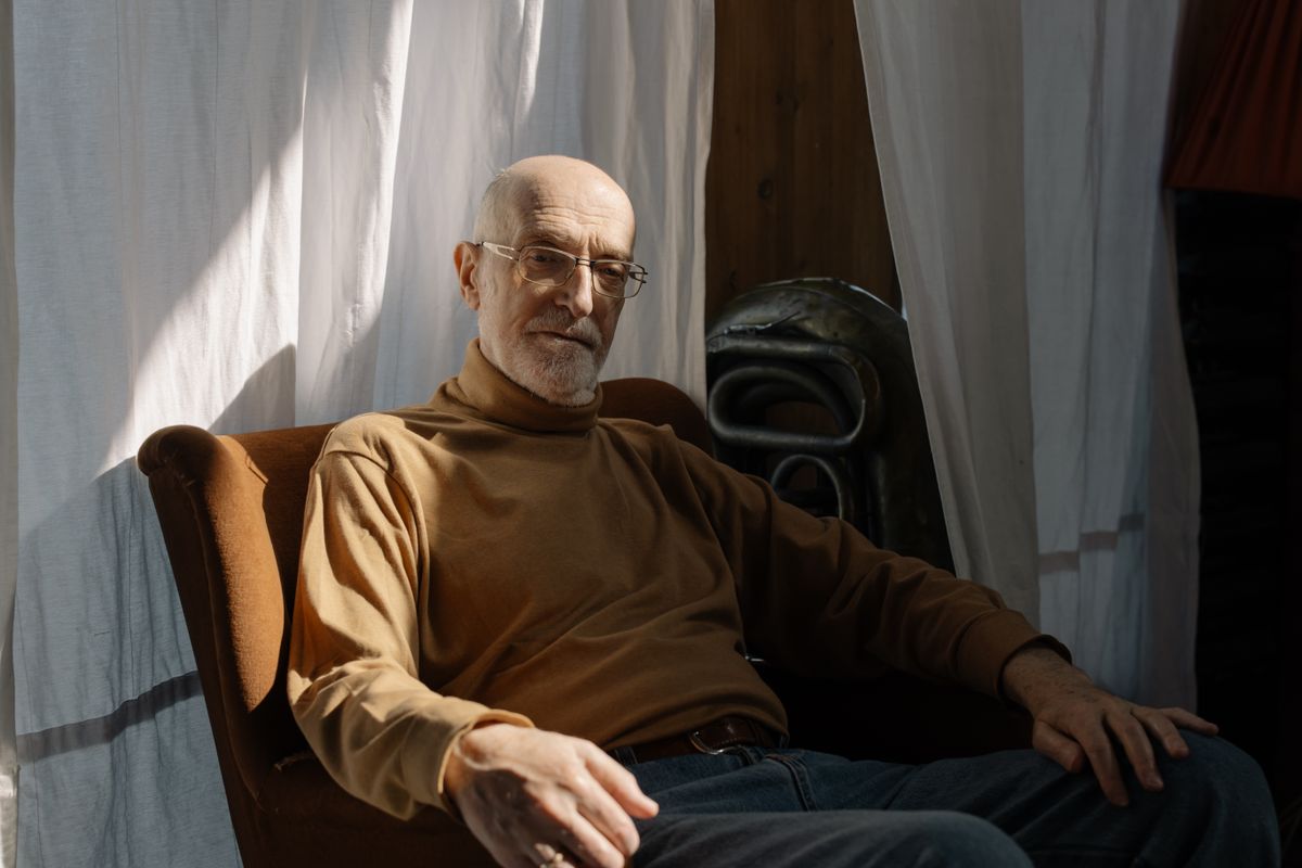 An older man seated comfortably in an armchair in a sunlit room