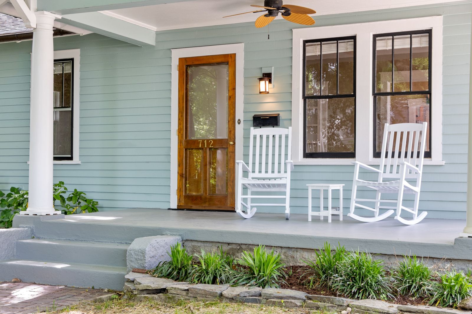 A covered front porch with two rocking chairs beside a wooden screen door