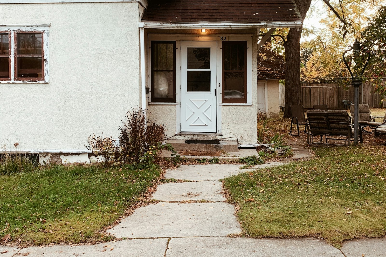 A concrete walk leading to the door of an older stucco house on an autumn afternoon