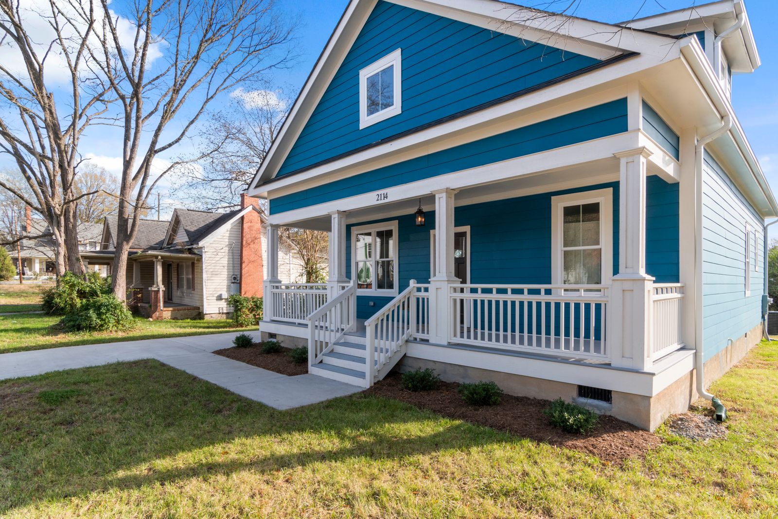 A blue bungalow with a white porch, railings, and steps leading to the front door