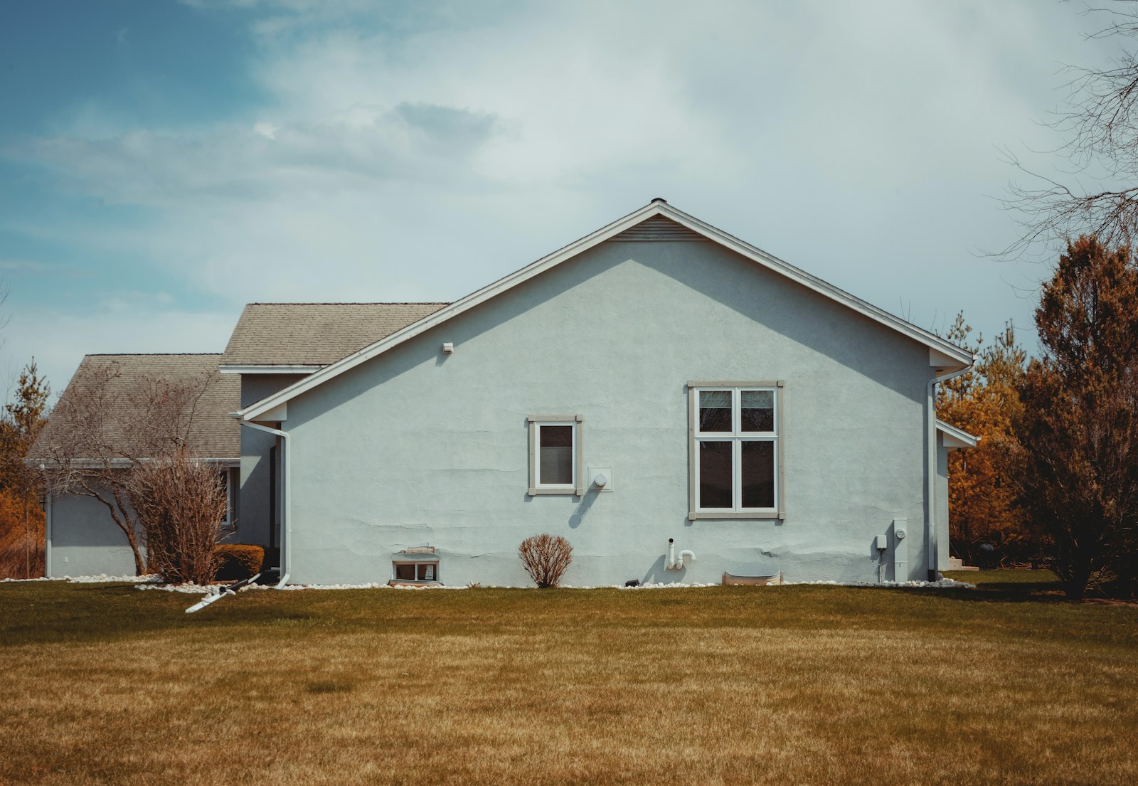 A single-story house with a pitched roof and an open lawn on an overcast day