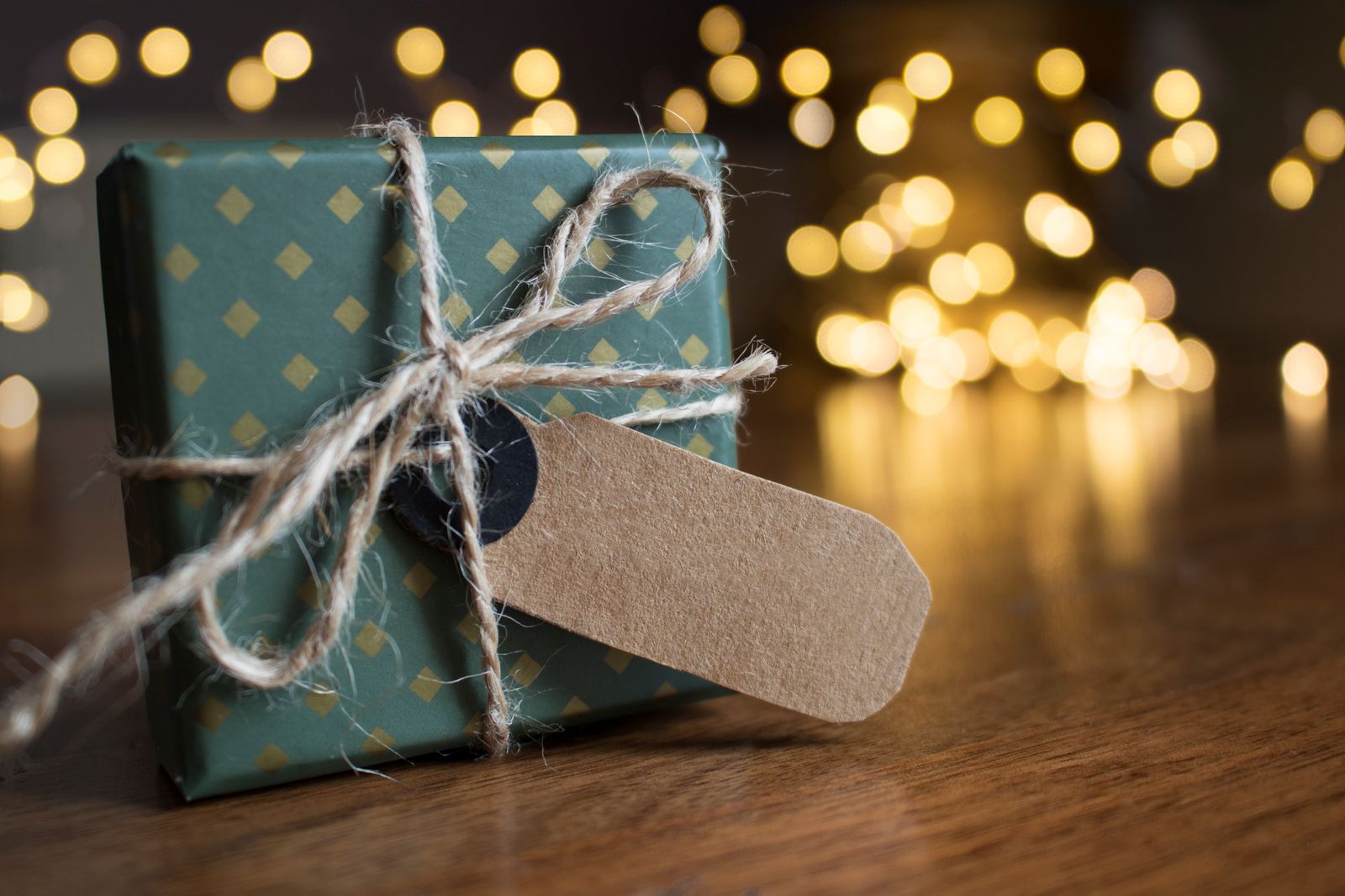 A small gift wrapped in green paper and tied with twine, its paper tag still blank, on a wooden table