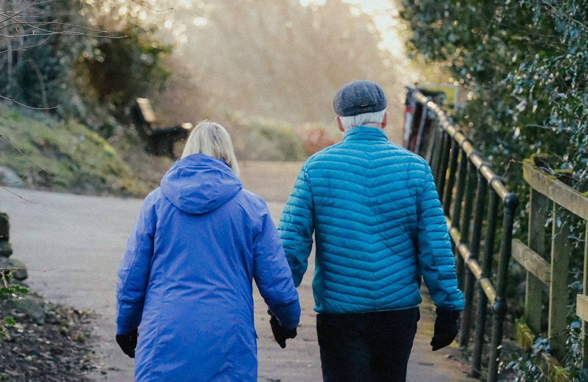 An older couple walking together outdoors on a park path