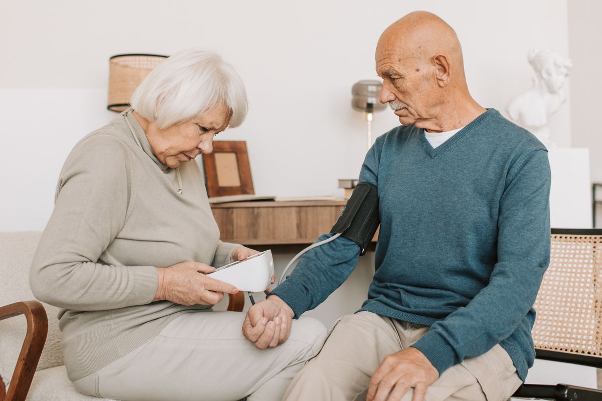 An older couple checking blood pressure at home with an upper-arm monitor