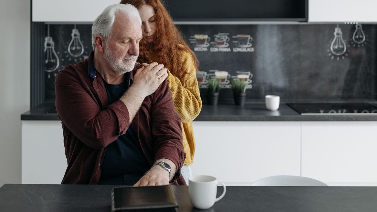 An adult daughter comforting her older father in the kitchen at home