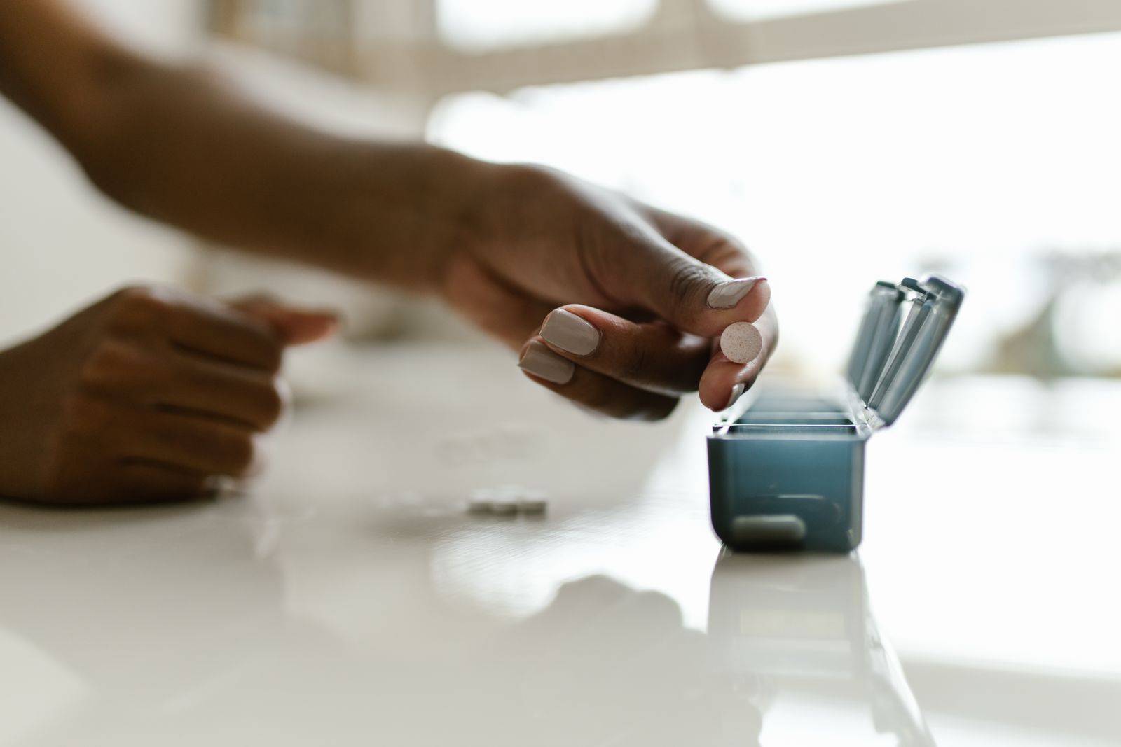 A hand sorting pills into a weekly pill organizer on a bright table, the simple system that prevents dosing mistakes