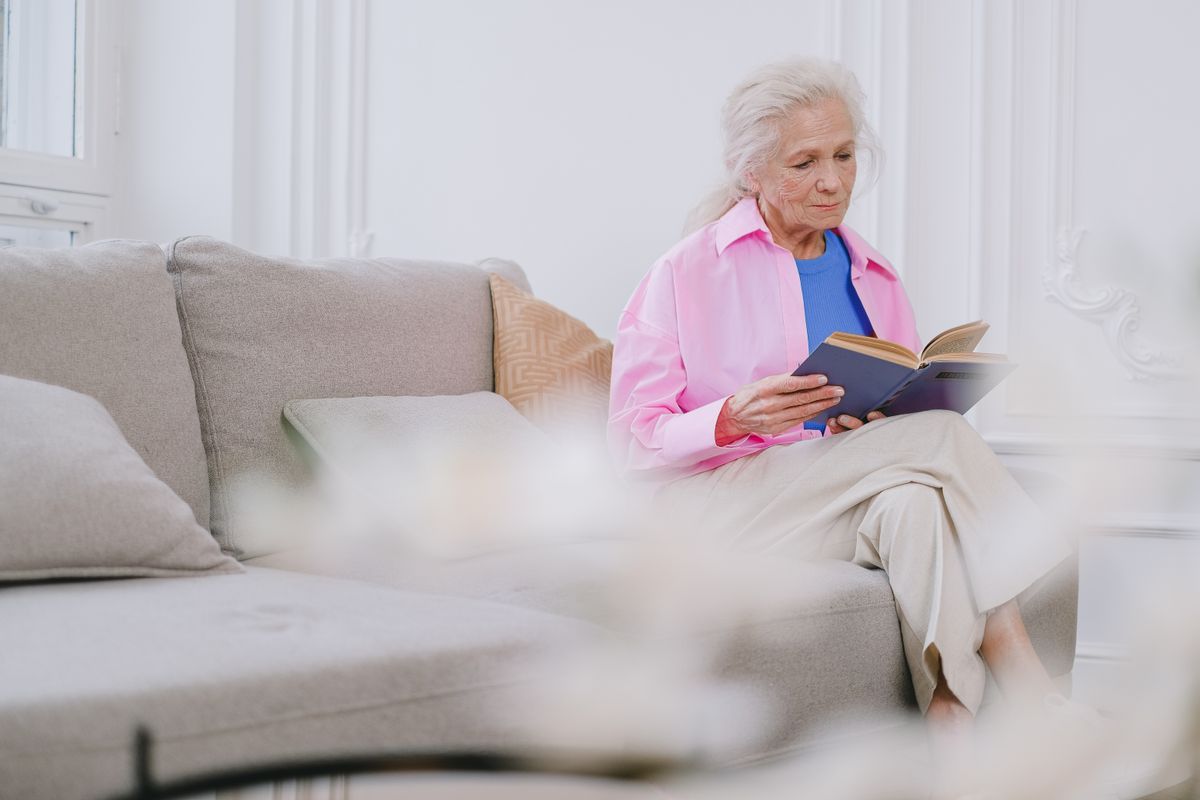 An older woman reading calmly in a bright living room, the kind of independent life at home that a medical alert system helps protect