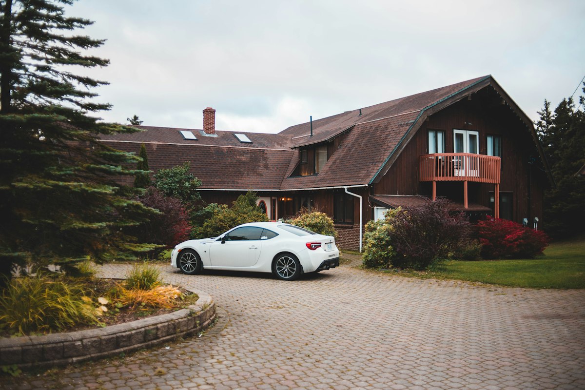 A white car parked on a paved driveway in front of a house on an overcast day