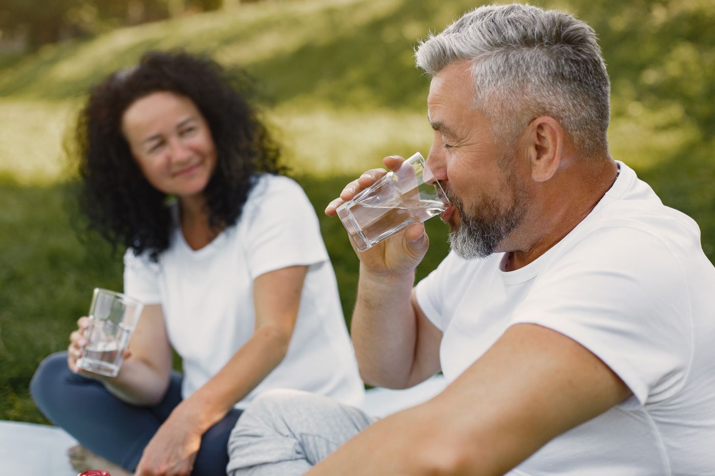 An older couple staying hydrated with glasses of water outdoors on a warm summer day